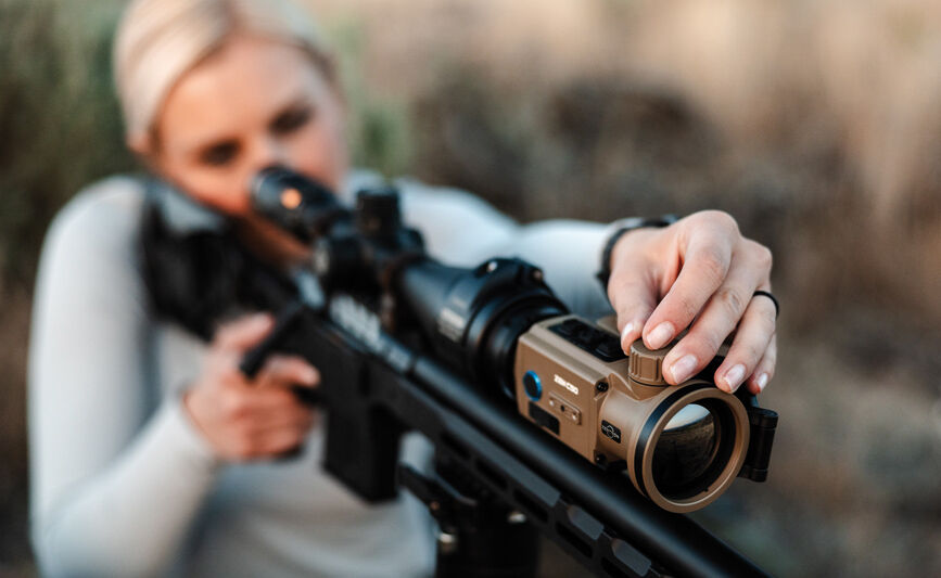 Frau justiert Zielfernrohr eines Gewehrs in natürlicher Umgebung